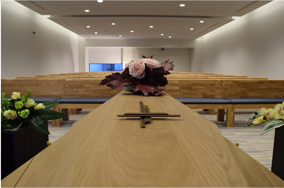 Houten uitvaartkist met bloemstuk in de aula