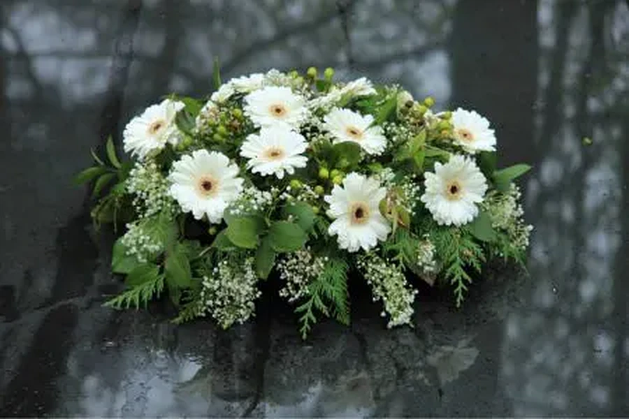 Wit rouwbloemstuk met gerbera's op een grafsteen