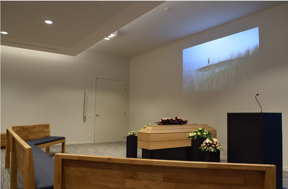 Aula met kist, bloemen, projectiescherm en houten zitbanken