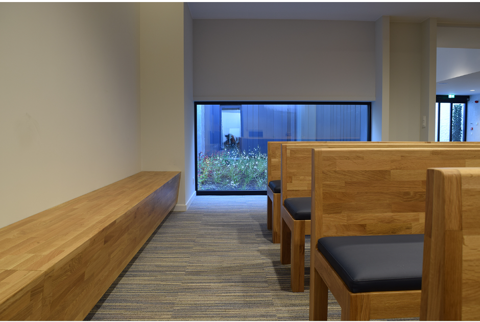 Houten zitbanken in de aula met zicht op een bloementuin