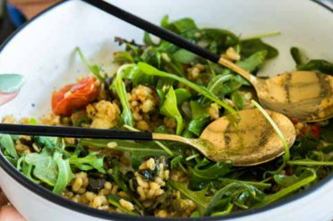 Schaal met salade van gerst, spinazie en tomaten met twee gouden serveerlepels