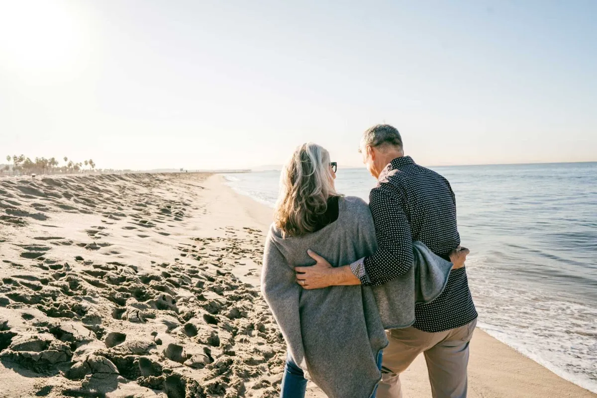 Ouder koppel wandelt samen op het strand bij zonsondergang